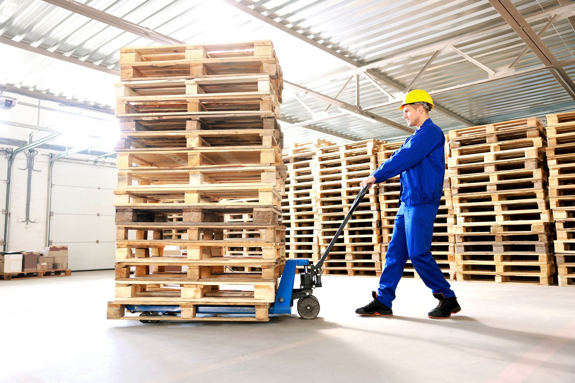 Worker moving a stack of wooden pallets in a warehouse
